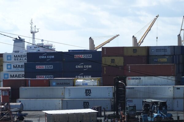 Stacked shipping containers and quay cranes at the Port of Douala in Cameroon, with a cargo ship behind