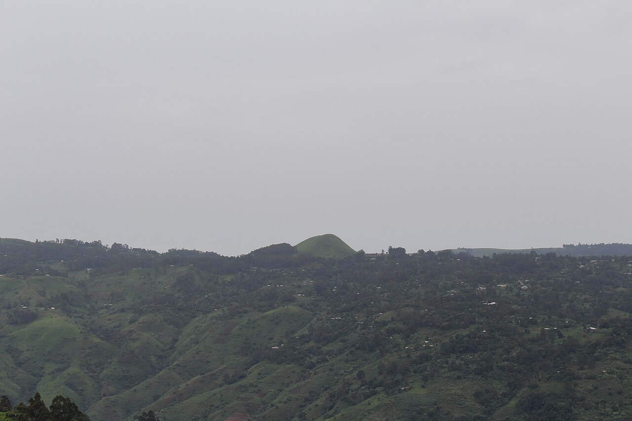 Green hills with scattered houses and a rounded peak under a grey sky in Cameroon's North-West region.