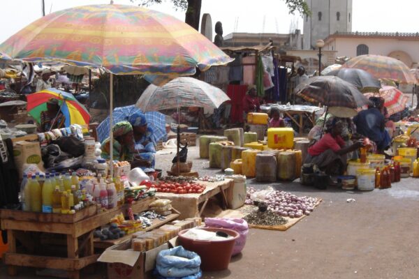 Women sell bottled oil, tomatoes, onions, soap and household goods under colourful parasols at a market in Foumban, Cameroon