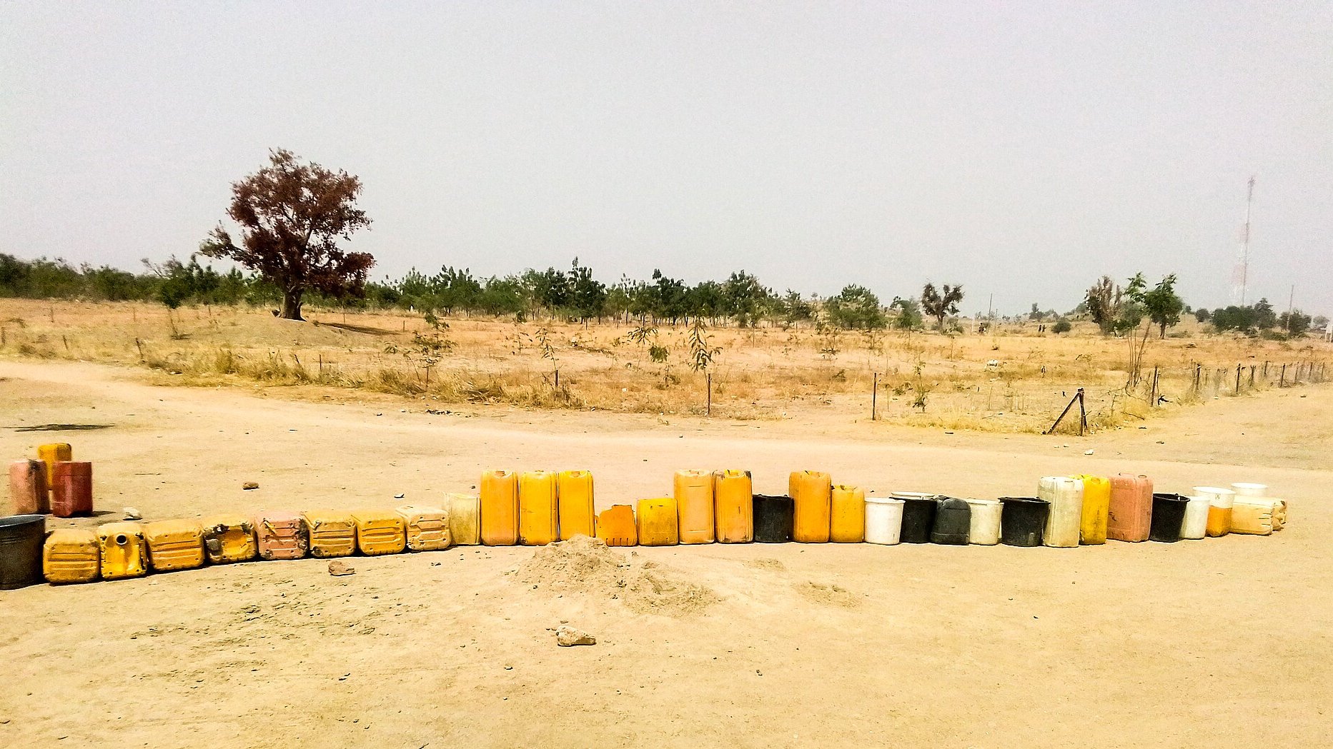 Line of yellow jerrycans and buckets set out on bare ground to wait for water at the Minawao refugee camp in northern Cameroon