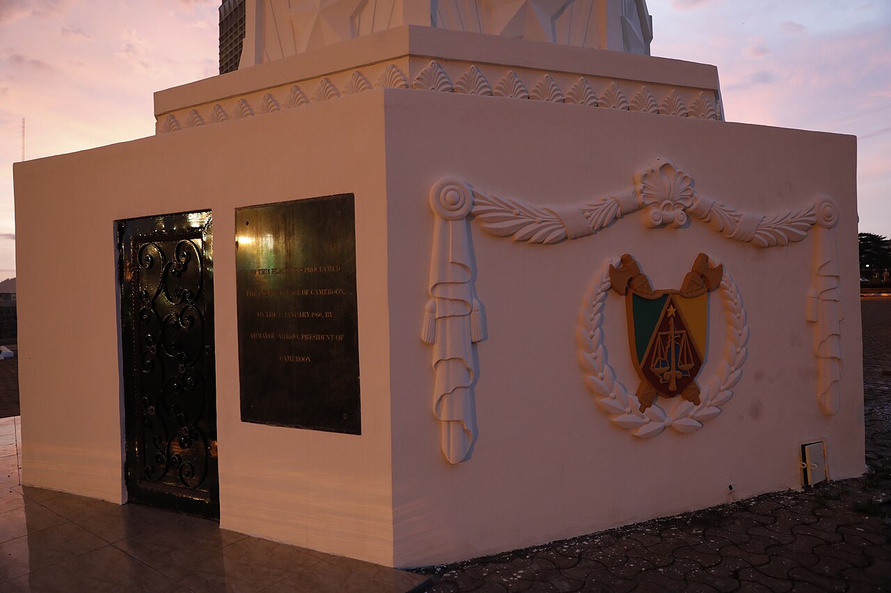 The base of the independence monument in Yaoundé, Cameroon, with a bronze plaque and the national coat of arms at dusk