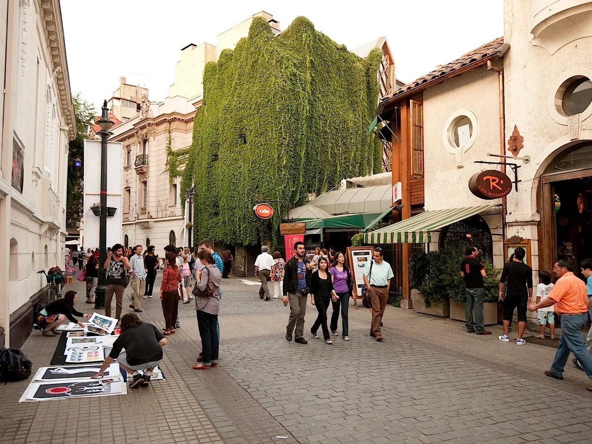 People walk along a pedestrian street lined with cafes and a building covered in ivy in central Santiago, Chile.