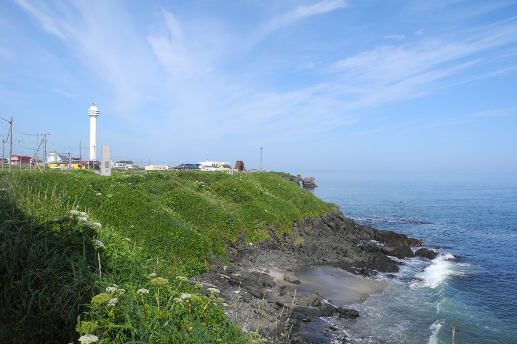 Grassy coastal cliffs and a white lighthouse tower at Cape Nosappu in Nemuro, Hokkaido, Japan