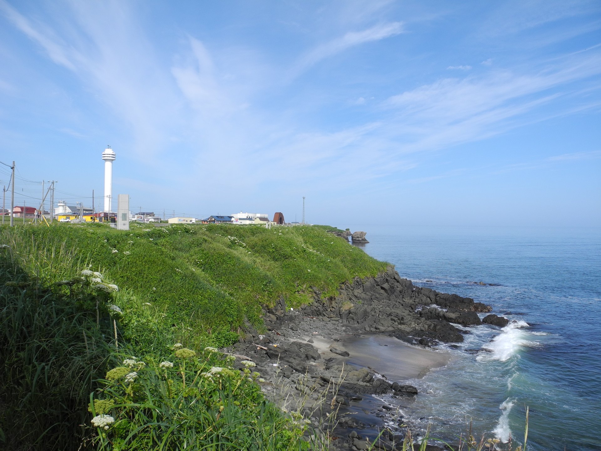 Grassy coastal cliffs and a white lighthouse tower at Cape Nosappu in Nemuro, Hokkaido, Japan