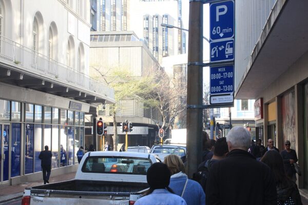 A busy street in central Cape Town with a white pickup truck in traffic, pedestrians on the pavement and a 60-minute parking sign on a pole