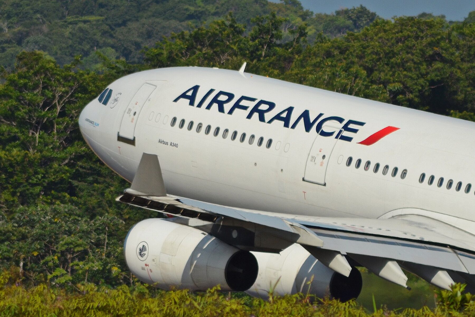 An Air France Airbus A340 climbs away from the runway at Cayenne airport in French Guiana, with dense green rainforest behind it