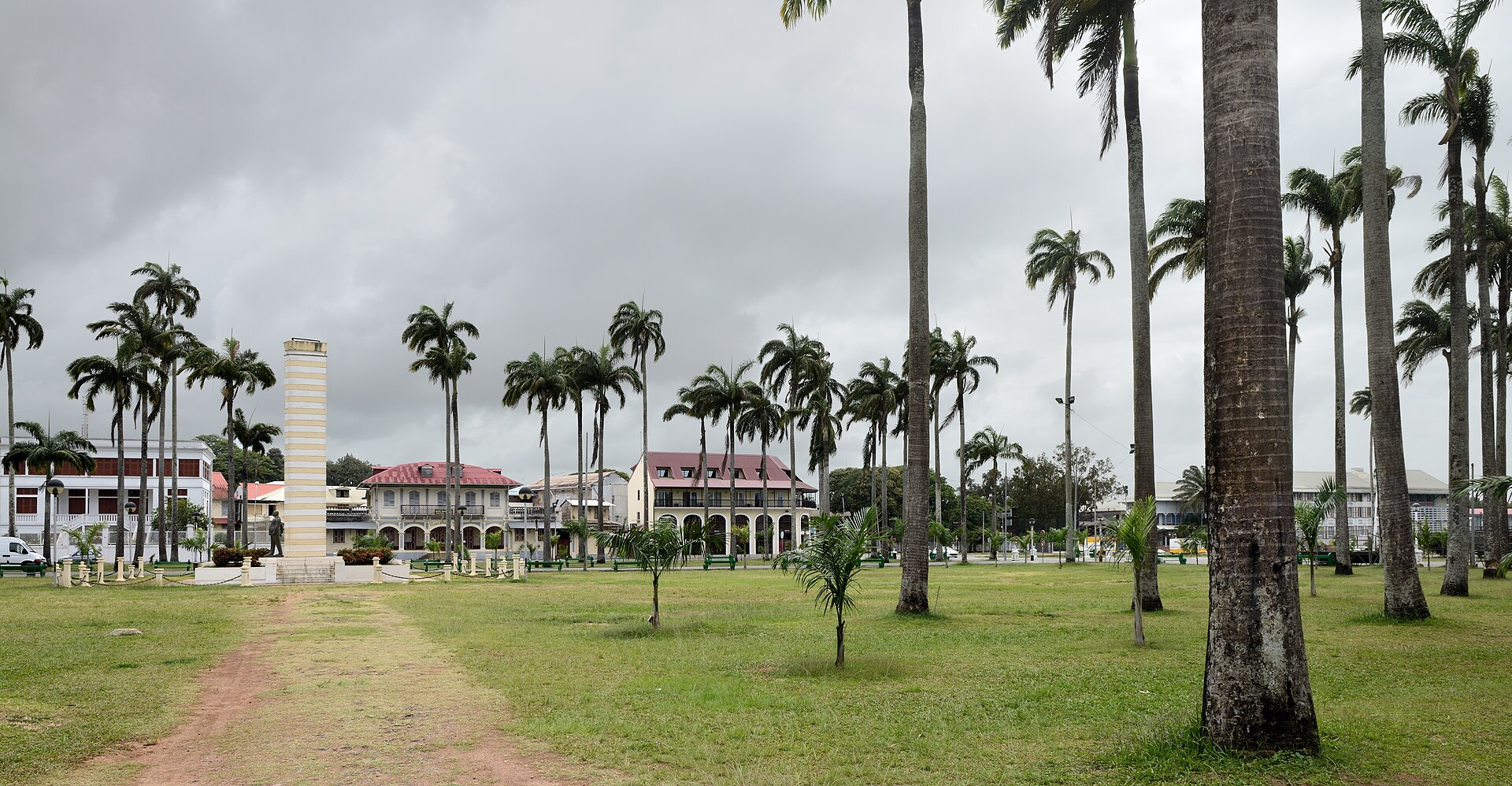 Tall royal palms around the Place des Palmistes, a public square in central Cayenne, French Guiana, under a cloudy sky