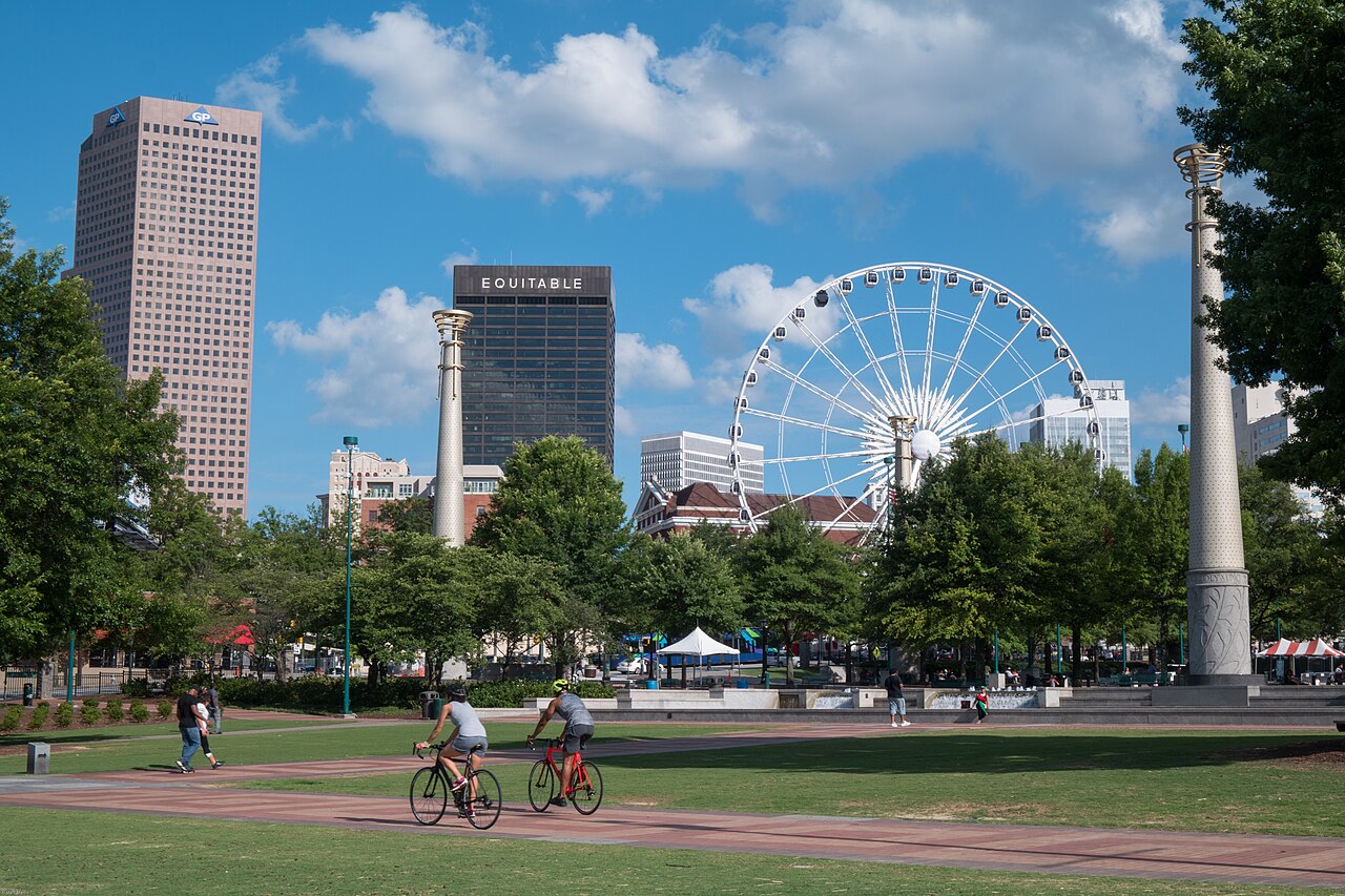 Cyclists in Centennial Olympic Park with downtown Atlanta towers and a Ferris wheel behind