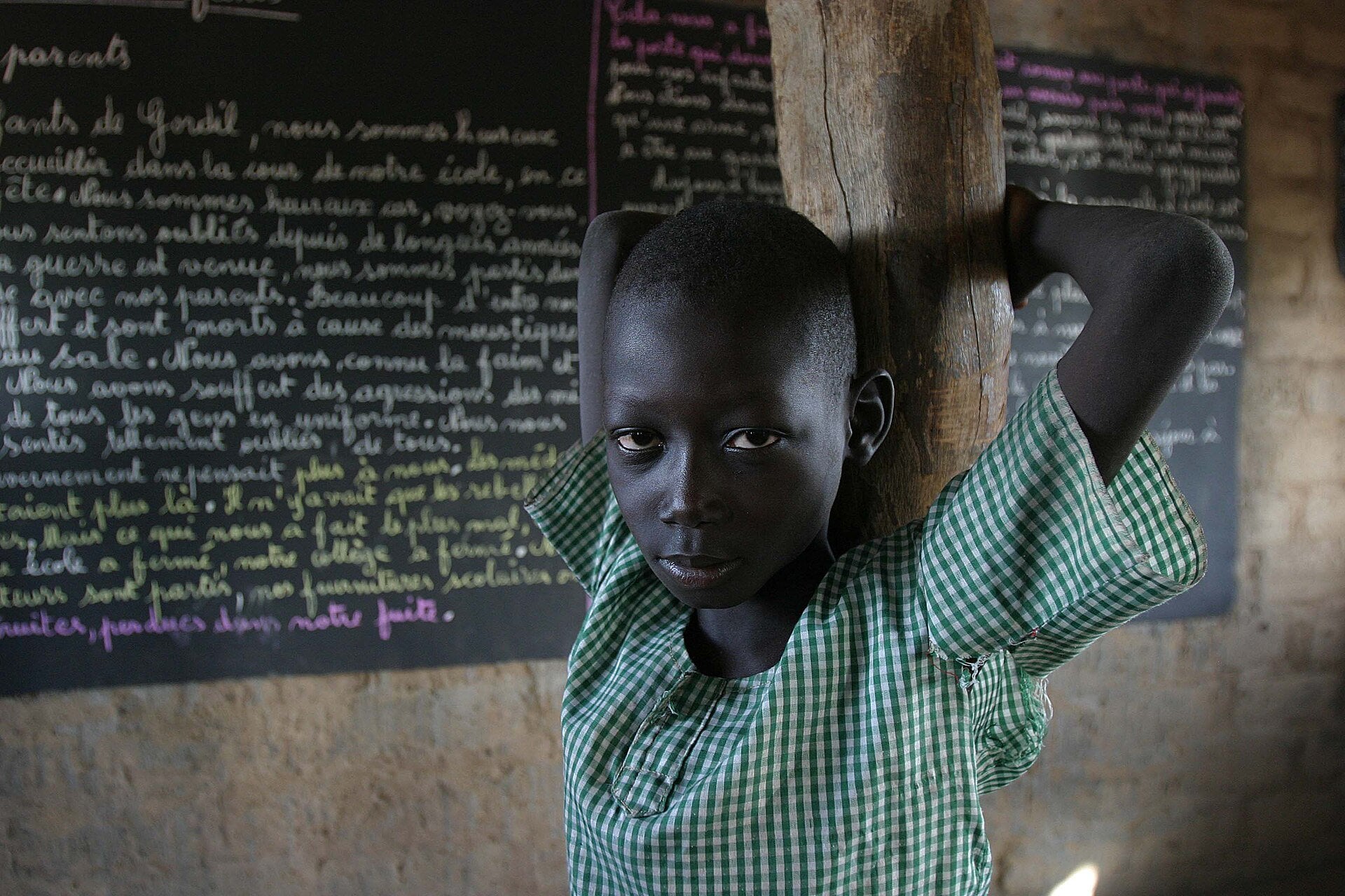 A schoolchild in a green checked shirt stands in a classroom in Gordil, northern Central African Republic, in front of a blackboard covered in French handwriting