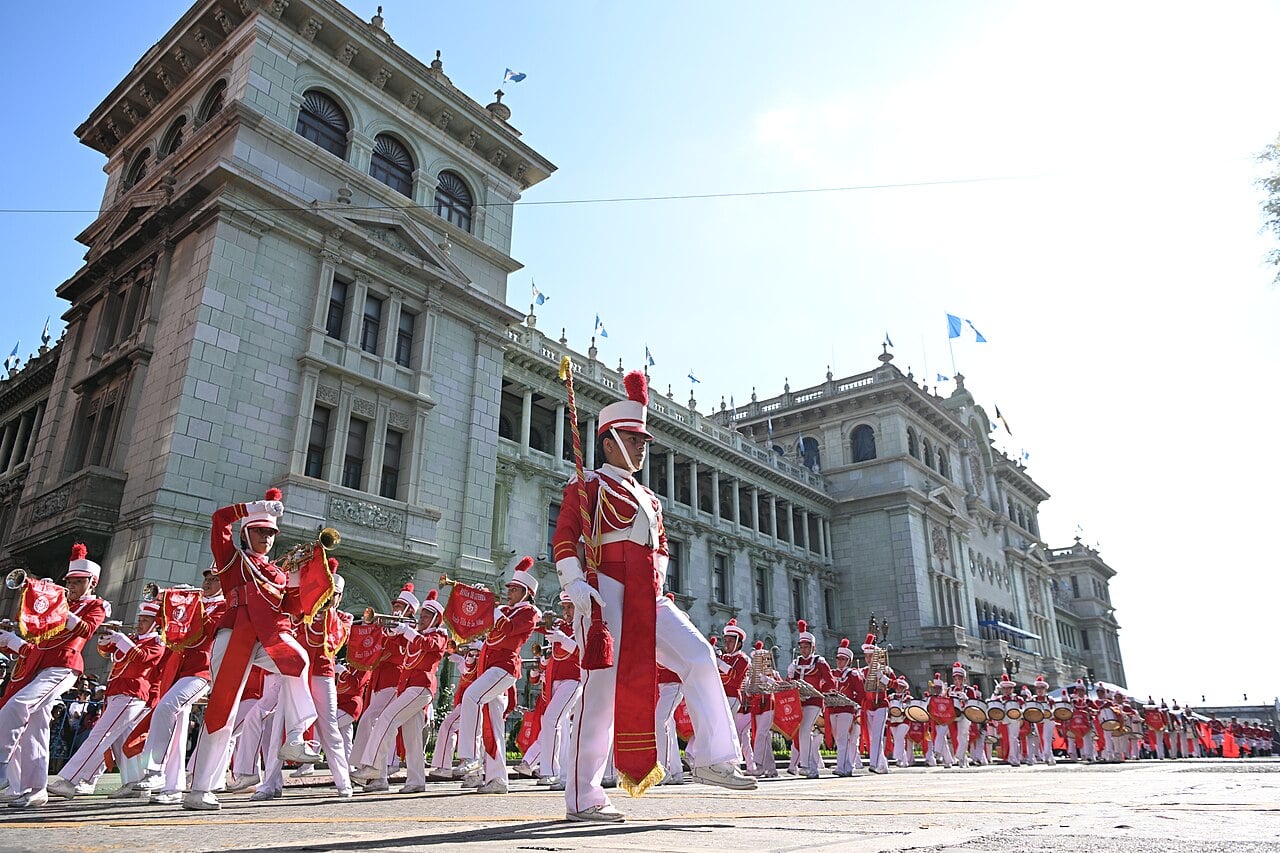 School band in red and white uniforms marching past the National Palace of Culture in Guatemala City