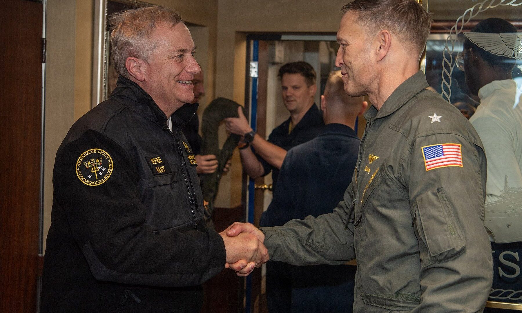 Chilean President José Antonio Kast in a Chilean Navy jacket shaking hands with a US Navy rear admiral aboard the USS Nimitz
