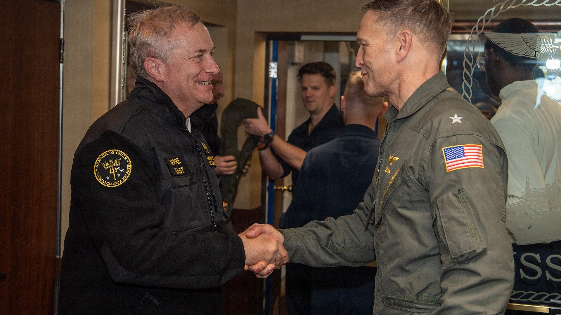 Chilean President José Antonio Kast in a Chilean Navy jacket shaking hands with a US Navy rear admiral aboard the USS Nimitz