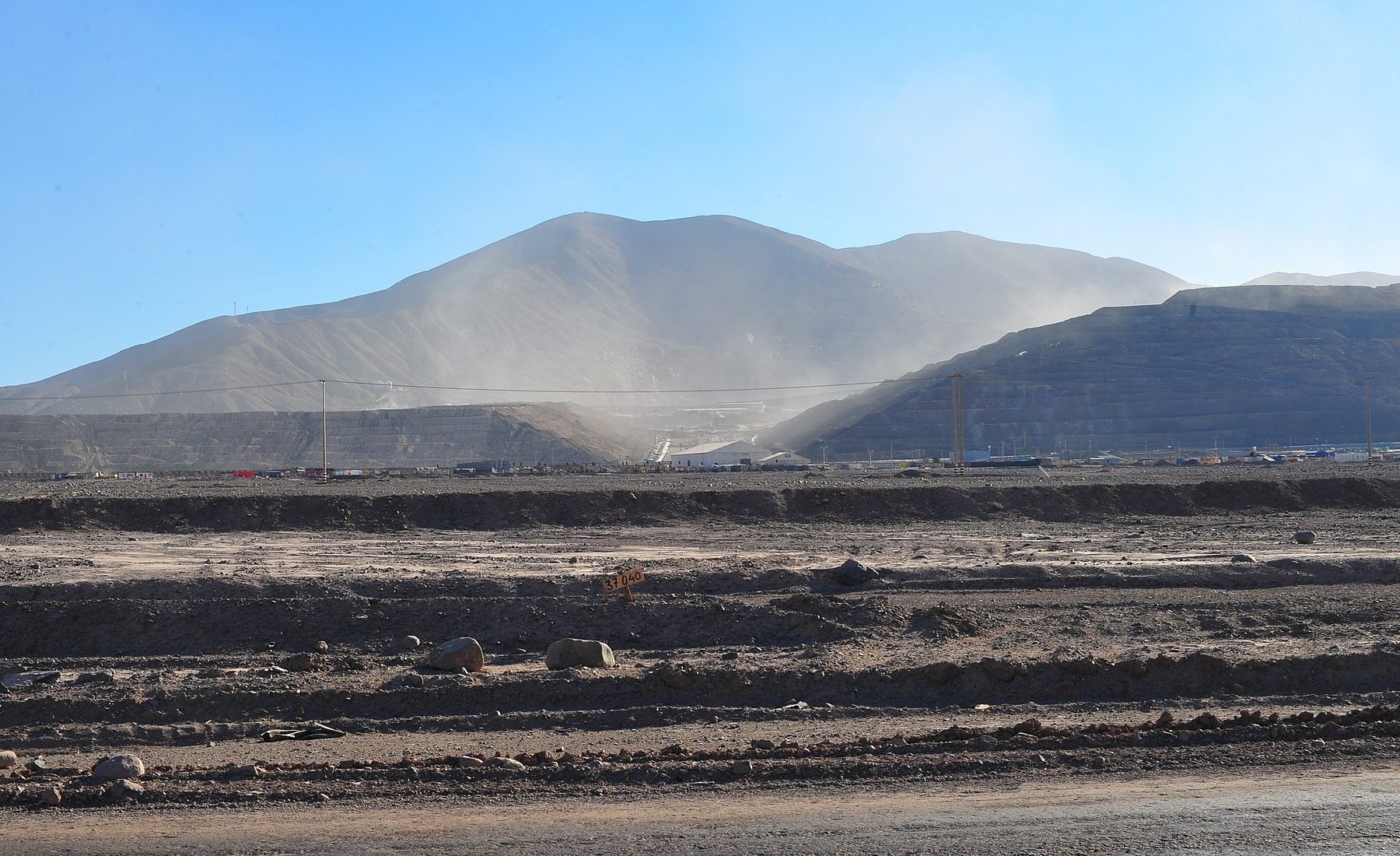 Dust rises over terraced waste dumps and a processing area at a large open-pit mine in northern Chile