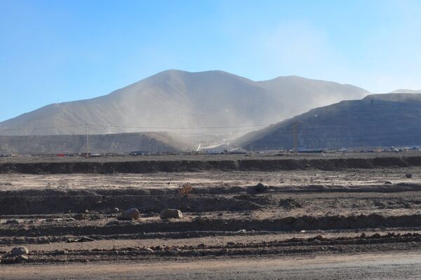 Dust rises over terraced waste dumps and a processing area at a large open-pit mine in northern Chile