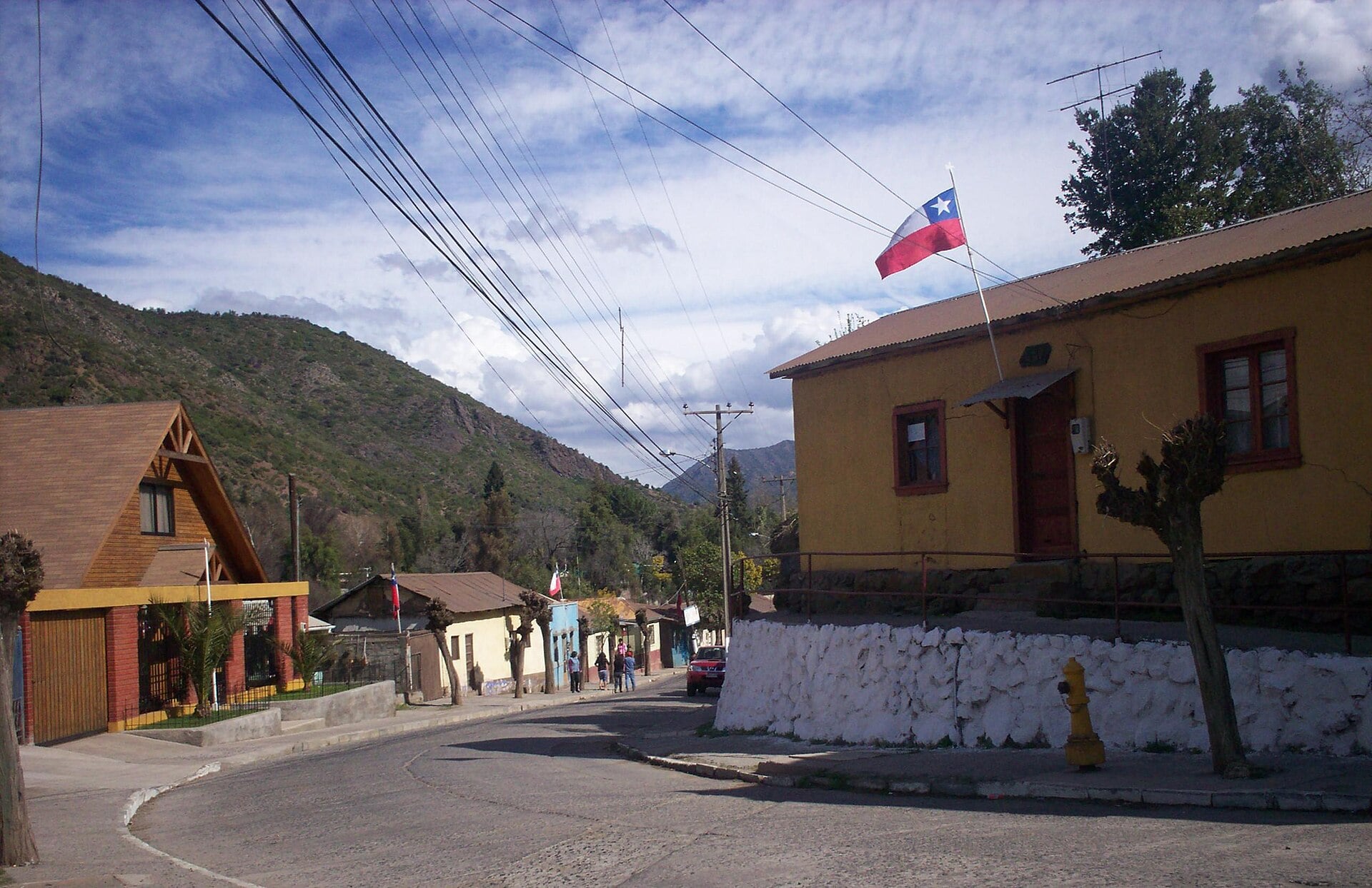 A street in Coya, in the Machalí commune of the O’Higgins region of Chile, with hills behind and a Chilean flag on a house