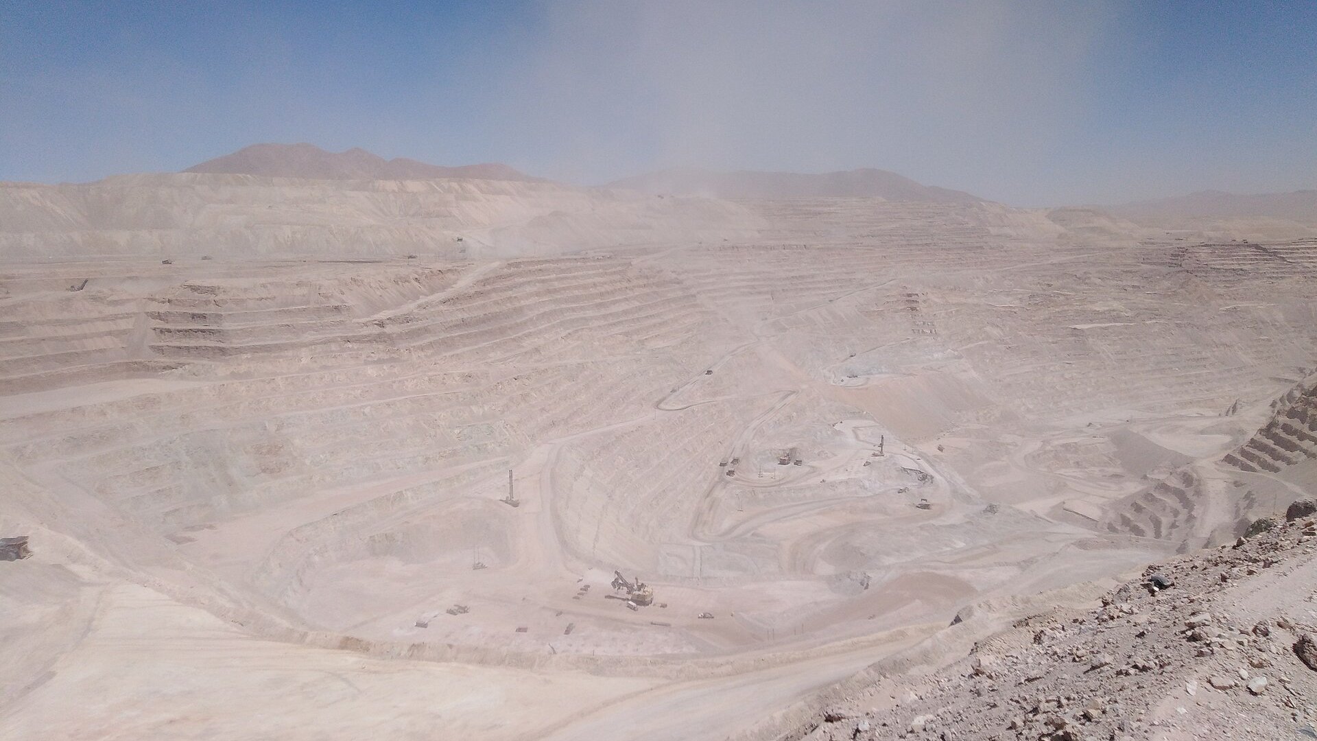 A wide terraced open-pit copper mine, Radomiro Tomic, in the dry hills of northern Chile under a hazy sky