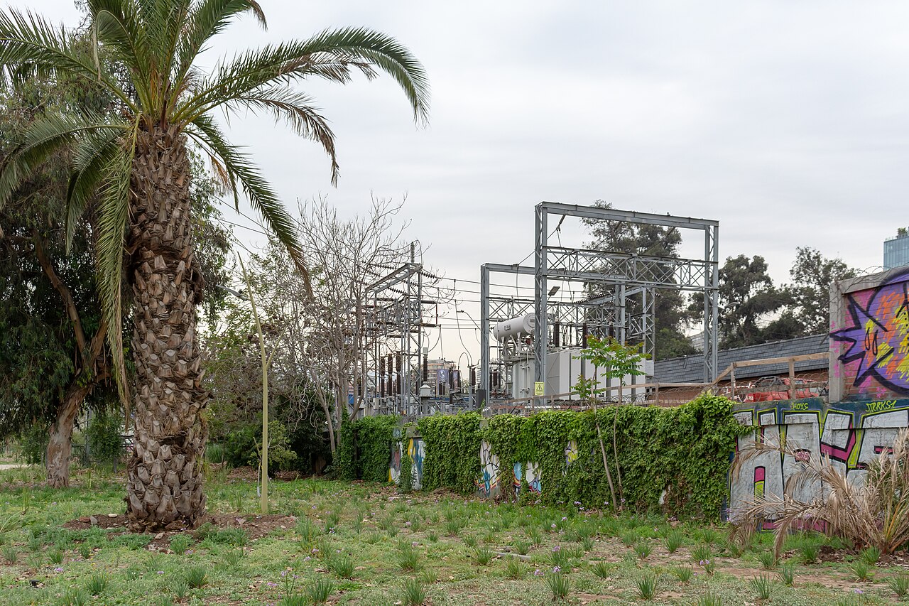 Electrical substation with transformers and steel frames behind a palm tree and graffiti wall in Las Condes, Santiago
