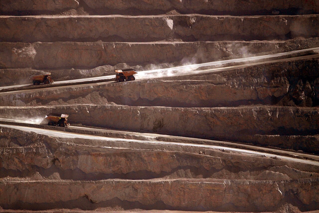 Yellow haul trucks climb dusty ramps between the terraced benches of the Escondida open-pit copper mine in northern Chile