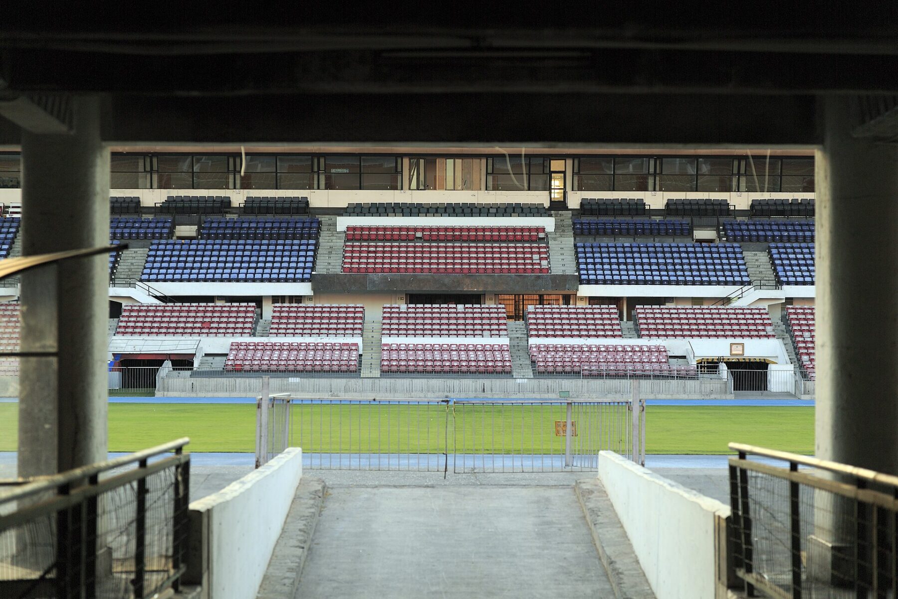 Red and blue seating stands of the Estadio Nacional in Santiago, Chile, seen from a tunnel entrance onto the pitch