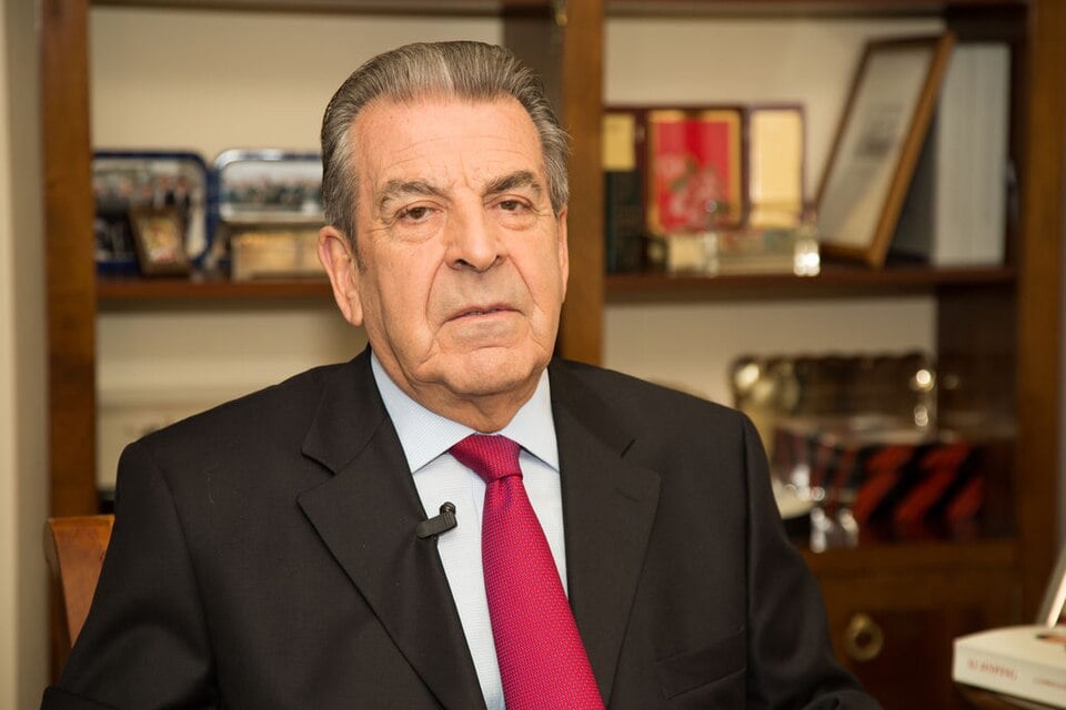 Eduardo Frei Ruiz-Tagle, grey-haired in a dark suit and red tie, seated in front of a bookshelf