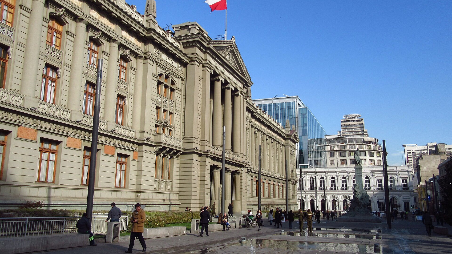 The Palace of Courts in Santiago, a grey stone courthouse with columns and a Chilean flag, seen from the plaza