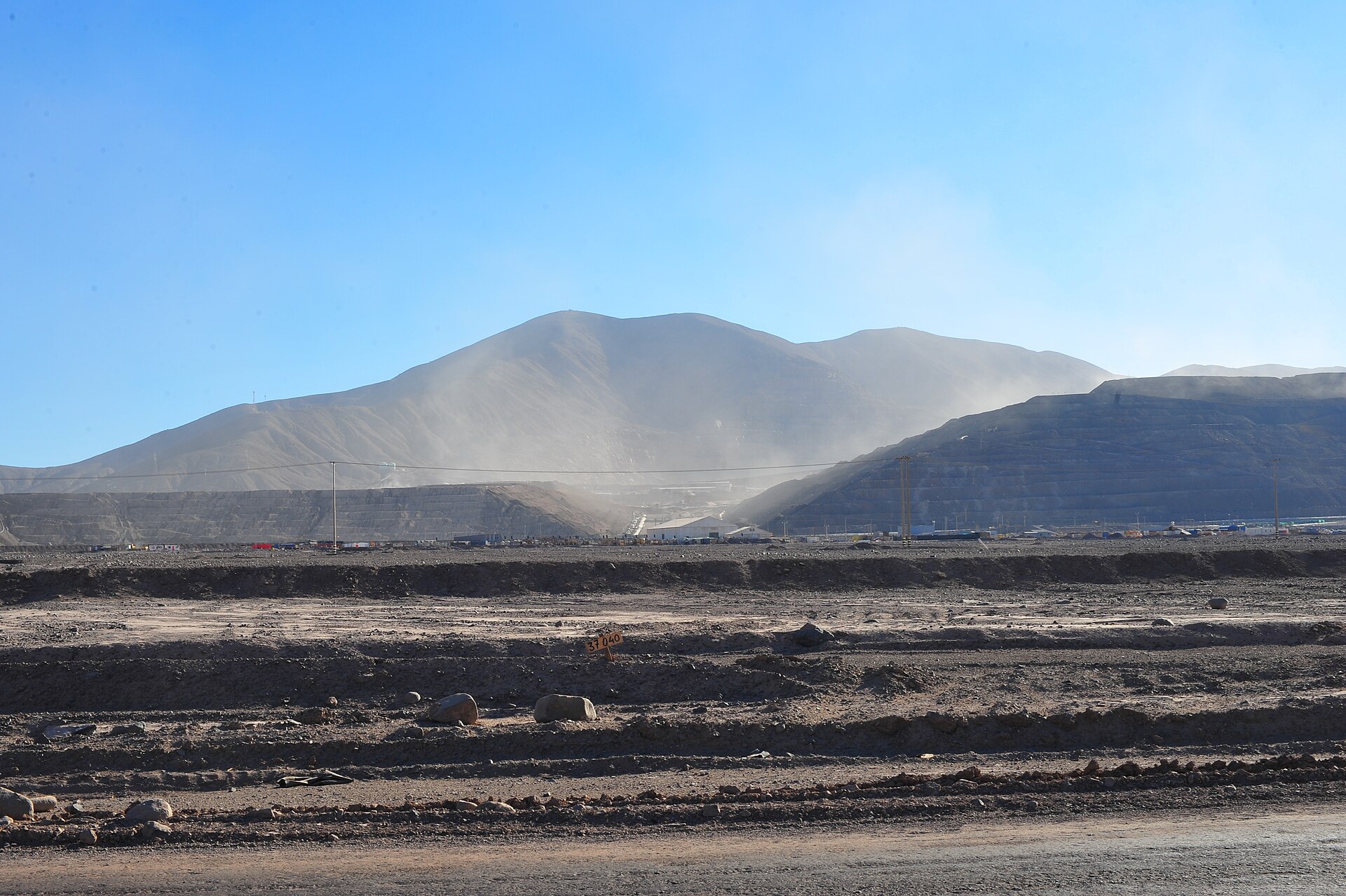 Dust rising from truck traffic at an open-pit copper mine with terraced walls in northern Chile