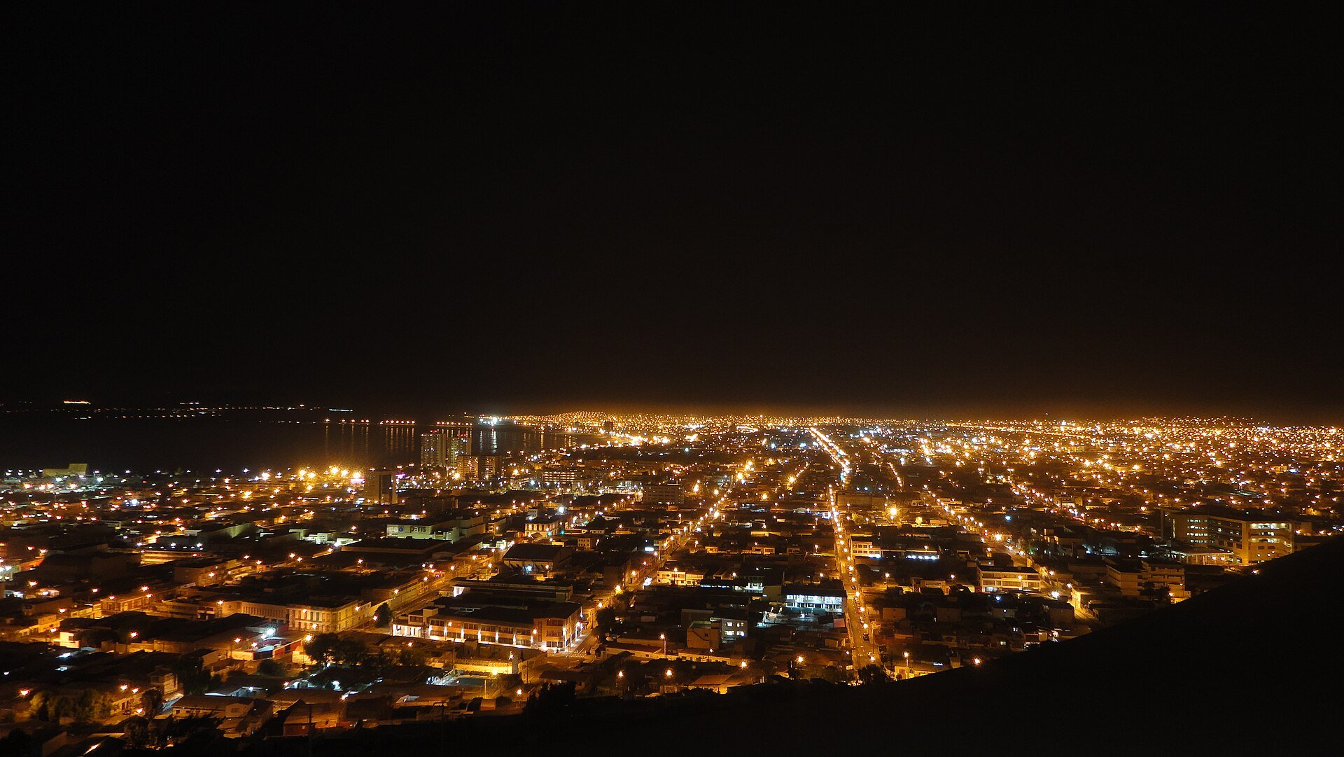 Night view of the lit-up city of Arica in northern Chile seen from the Morro headland, with the Pacific coast beyond