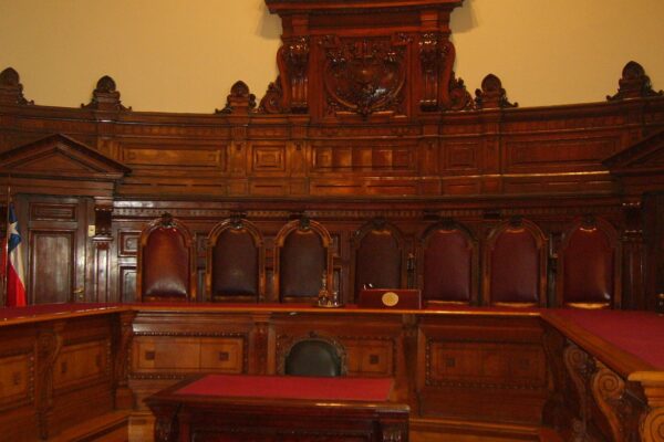 The wood-paneled full-court hearing room of Chile's Supreme Court in Santiago, with high-backed leather chairs and a Chilean flag