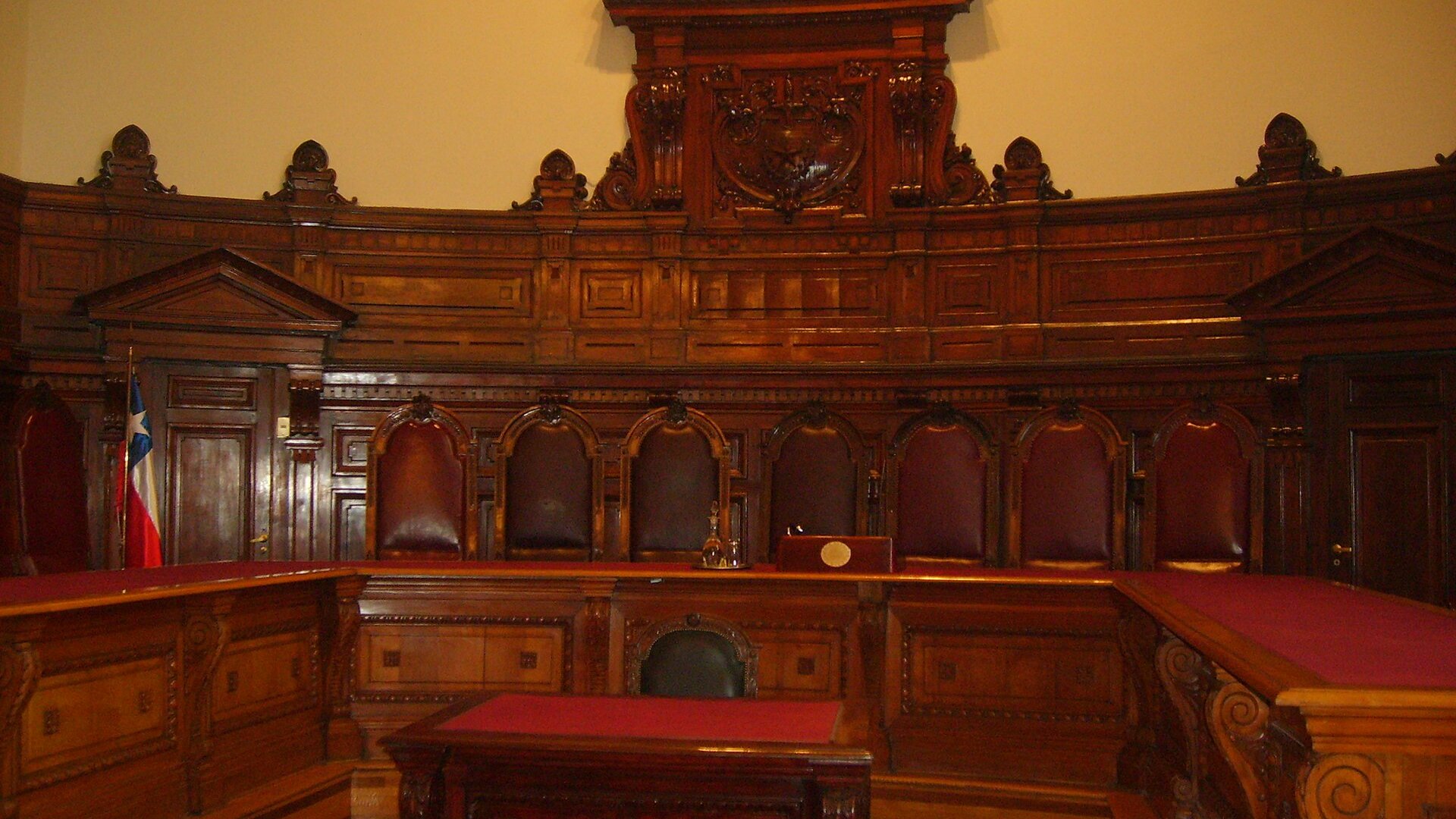 The wood-paneled full-court hearing room of Chile's Supreme Court in Santiago, with high-backed leather chairs and a Chilean flag