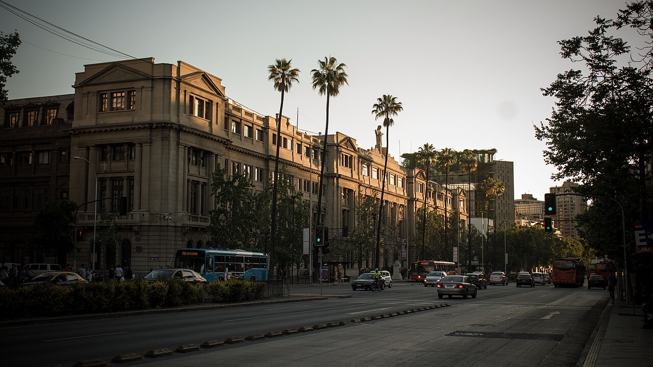 The Casa Central of the Pontifical Catholic University of Chile on the Alameda avenue in Santiago, with palm trees and buses in front