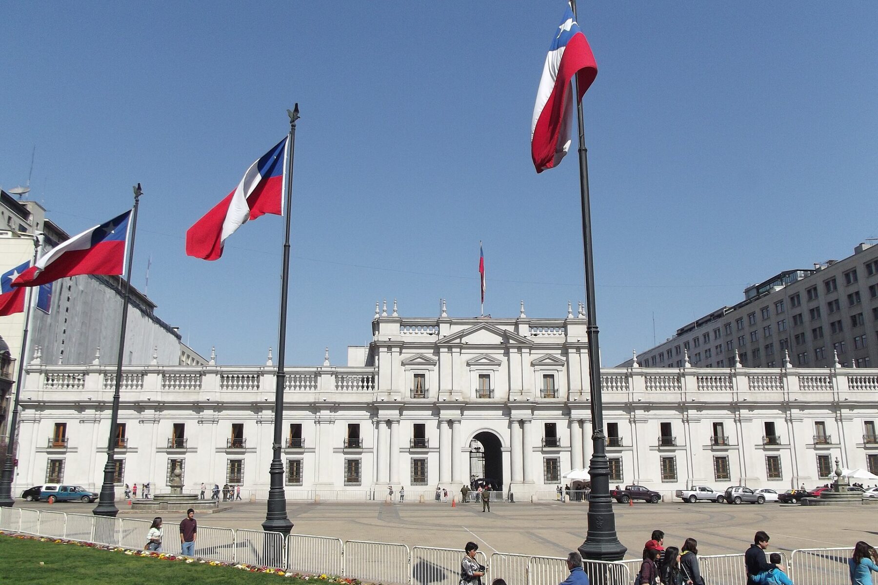 The white neoclassical facade of La Moneda Palace in Santiago, Chile, seen behind three Chilean flags