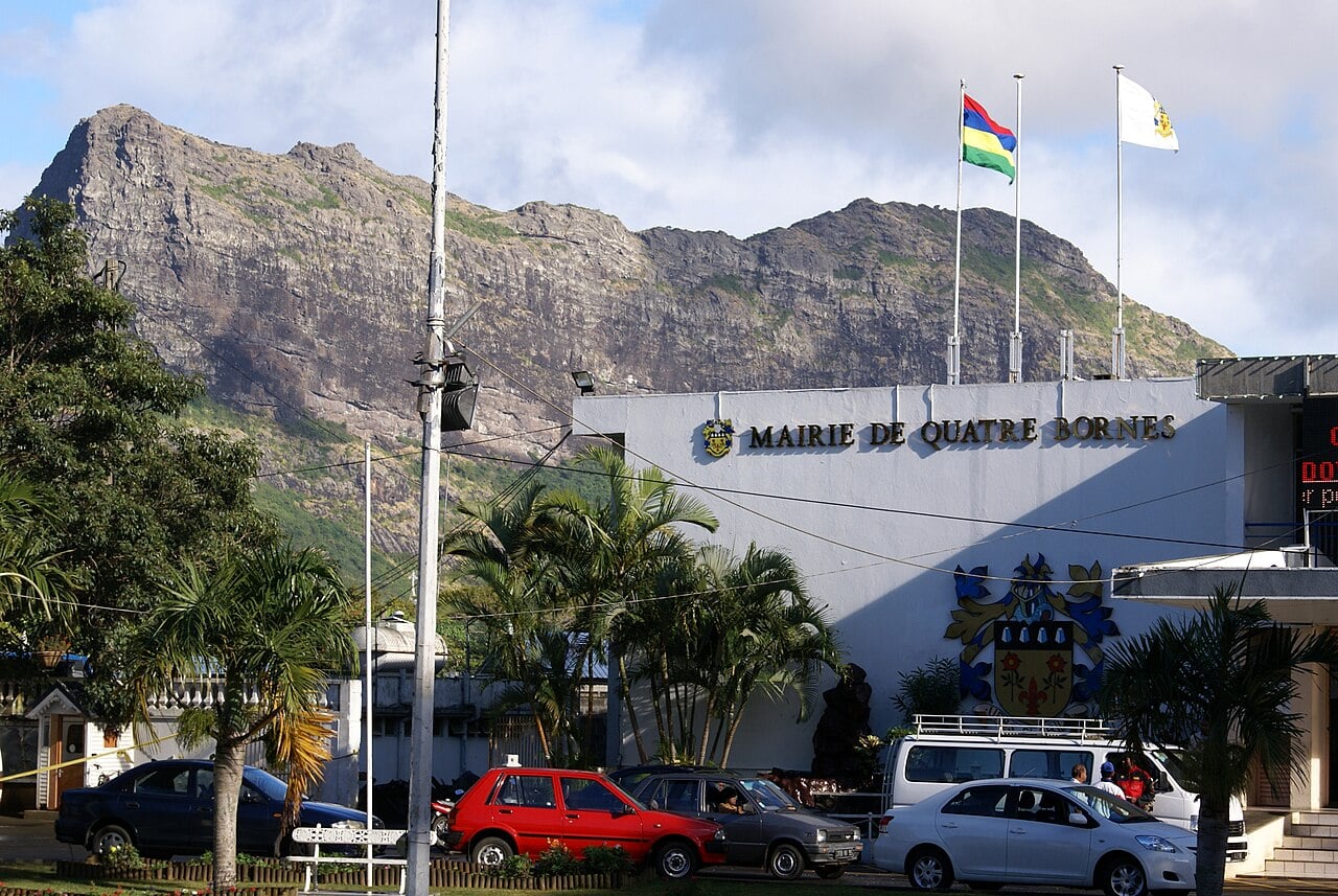 The Quatre Bornes town hall in Mauritius with the national flag and a rocky mountain ridge behind it.