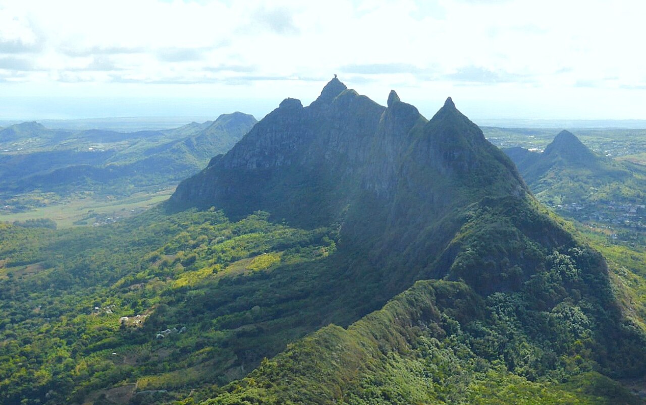 Aerial view of the jagged green peak of Pieter Both in central Mauritius, with farmland and hills below.