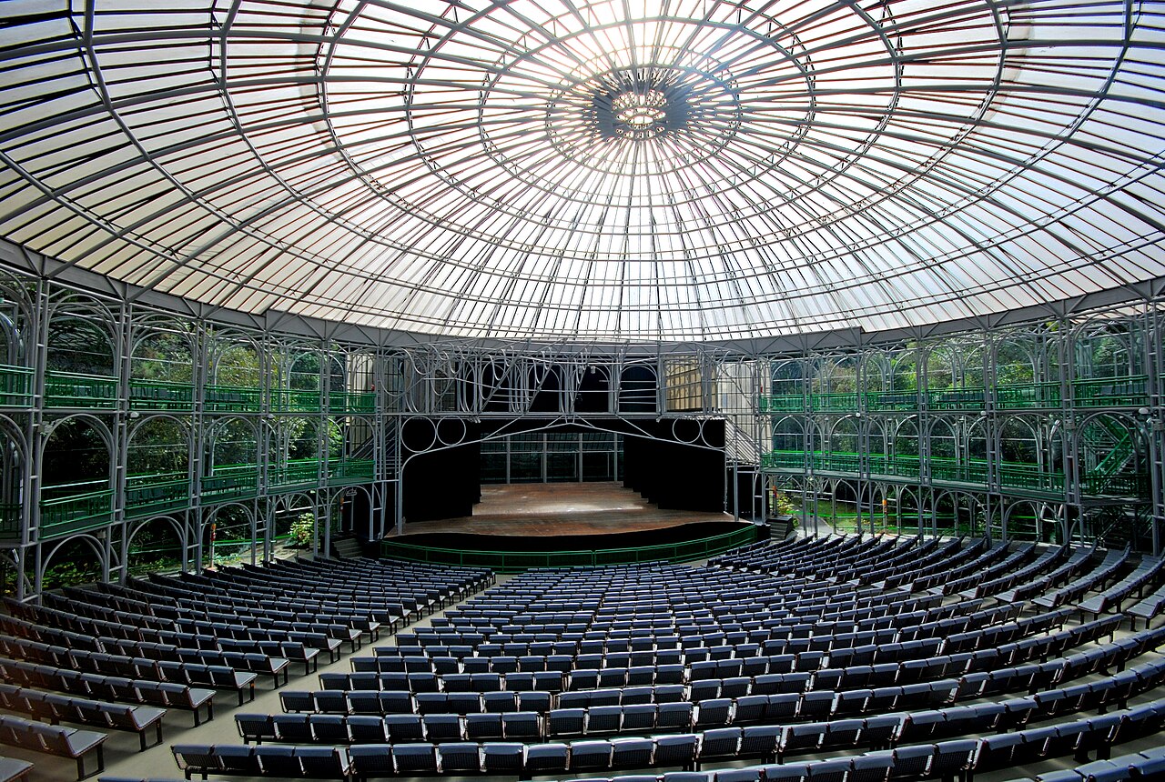 Interior of the Ópera de Arame in Curitiba, a steel-and-glass theater with rows of seats facing a stage under a translucent domed roof.