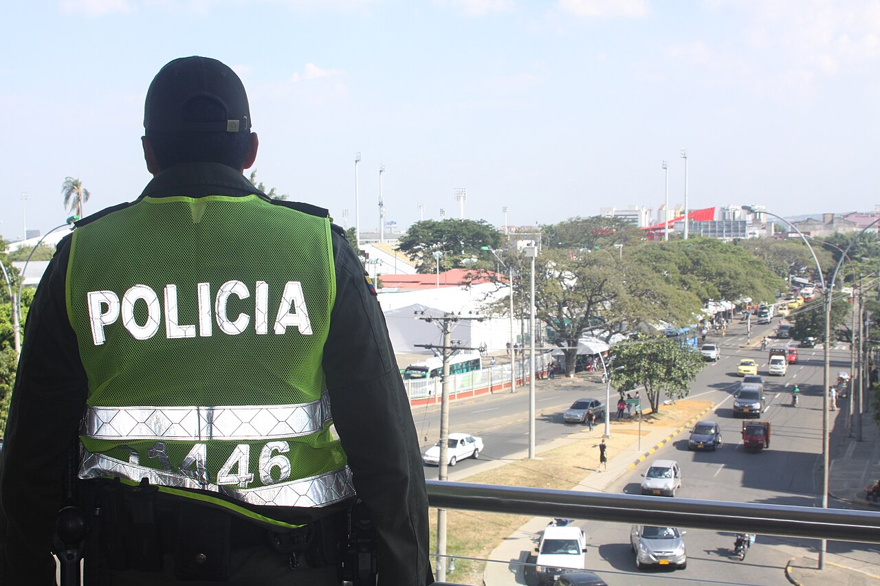 A Colombian National Police officer in a high-visibility vest watches over a busy avenue in Cali from a pedestrian bridge