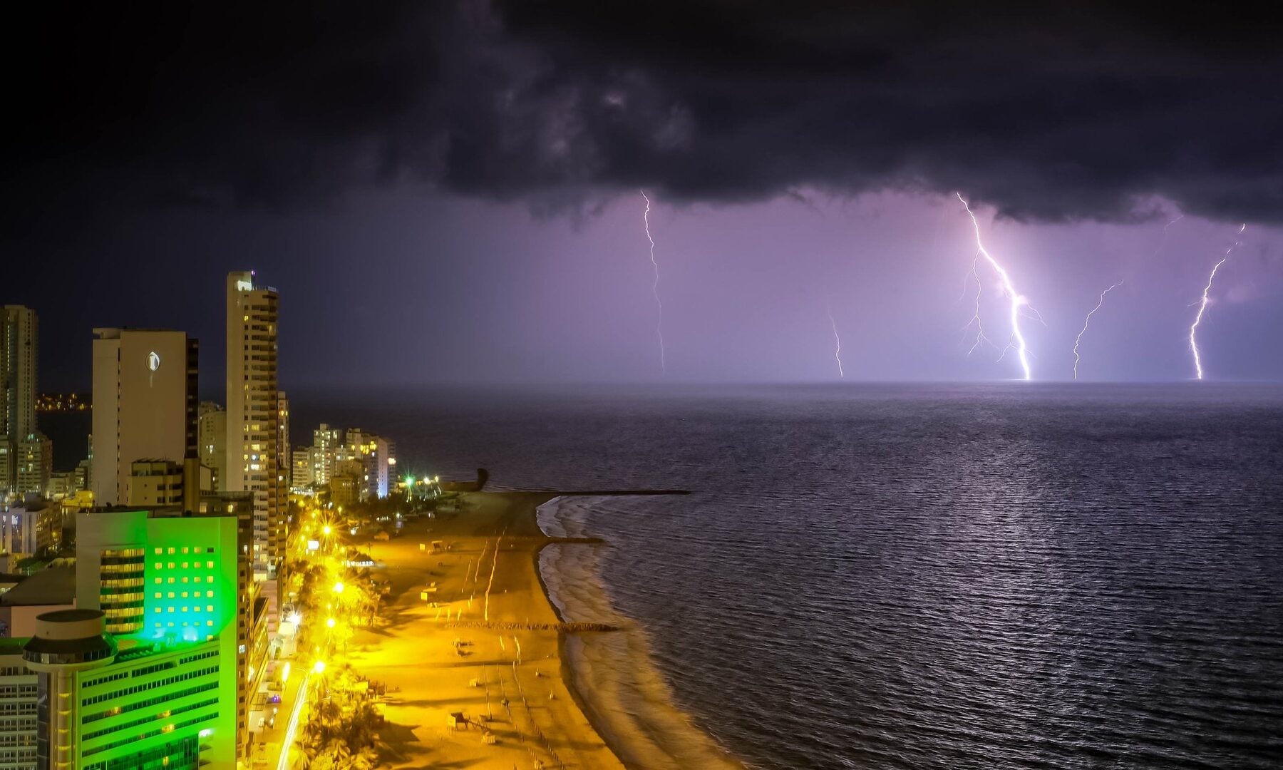 Lightning bolts over the Caribbean Sea beside the high-rise skyline and beach of Cartagena, Colombia, at night
