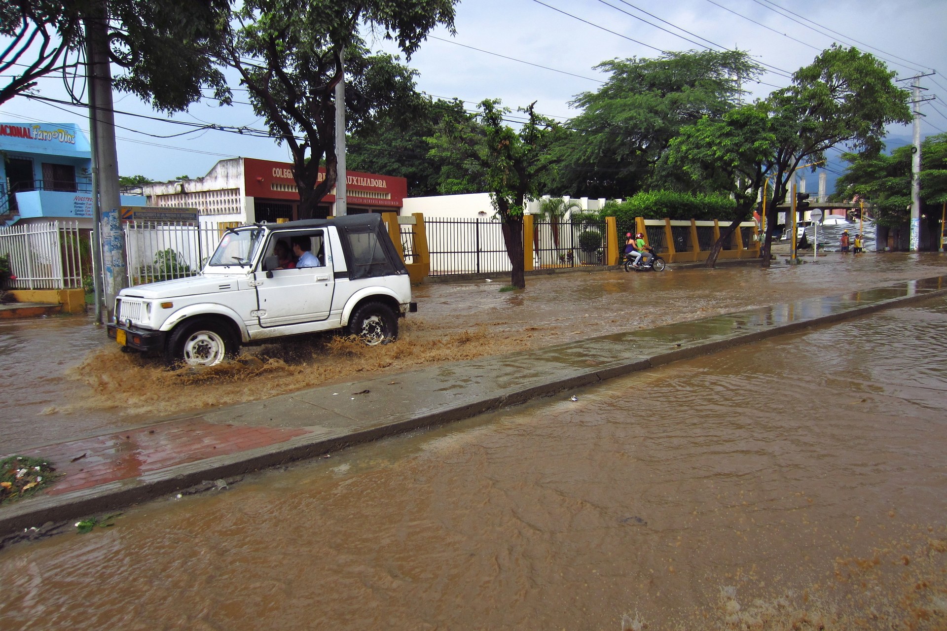 A white jeep drives through brown floodwater on a street in Santa Marta, Colombia