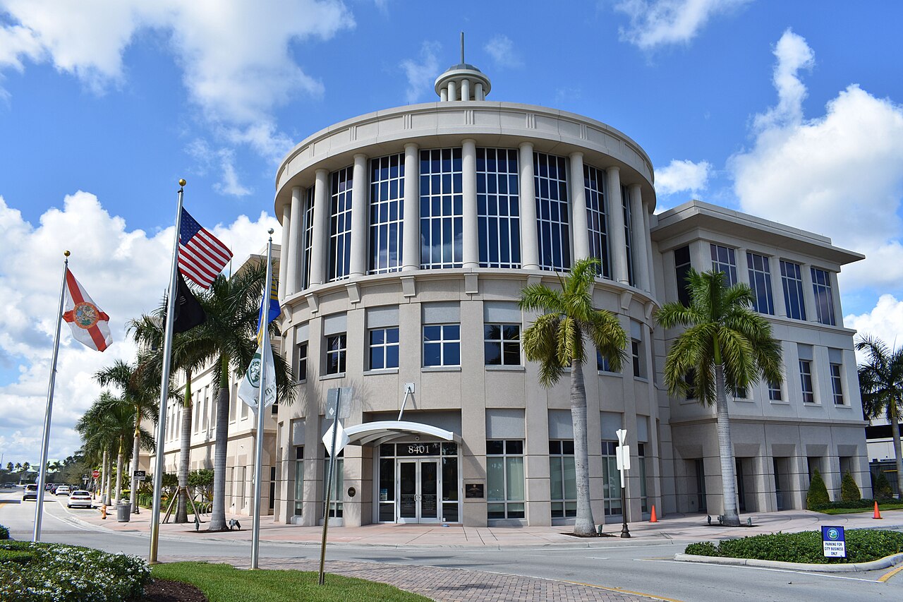 Round glass-and-stone city government building in Doral, Florida, with palm trees and flags