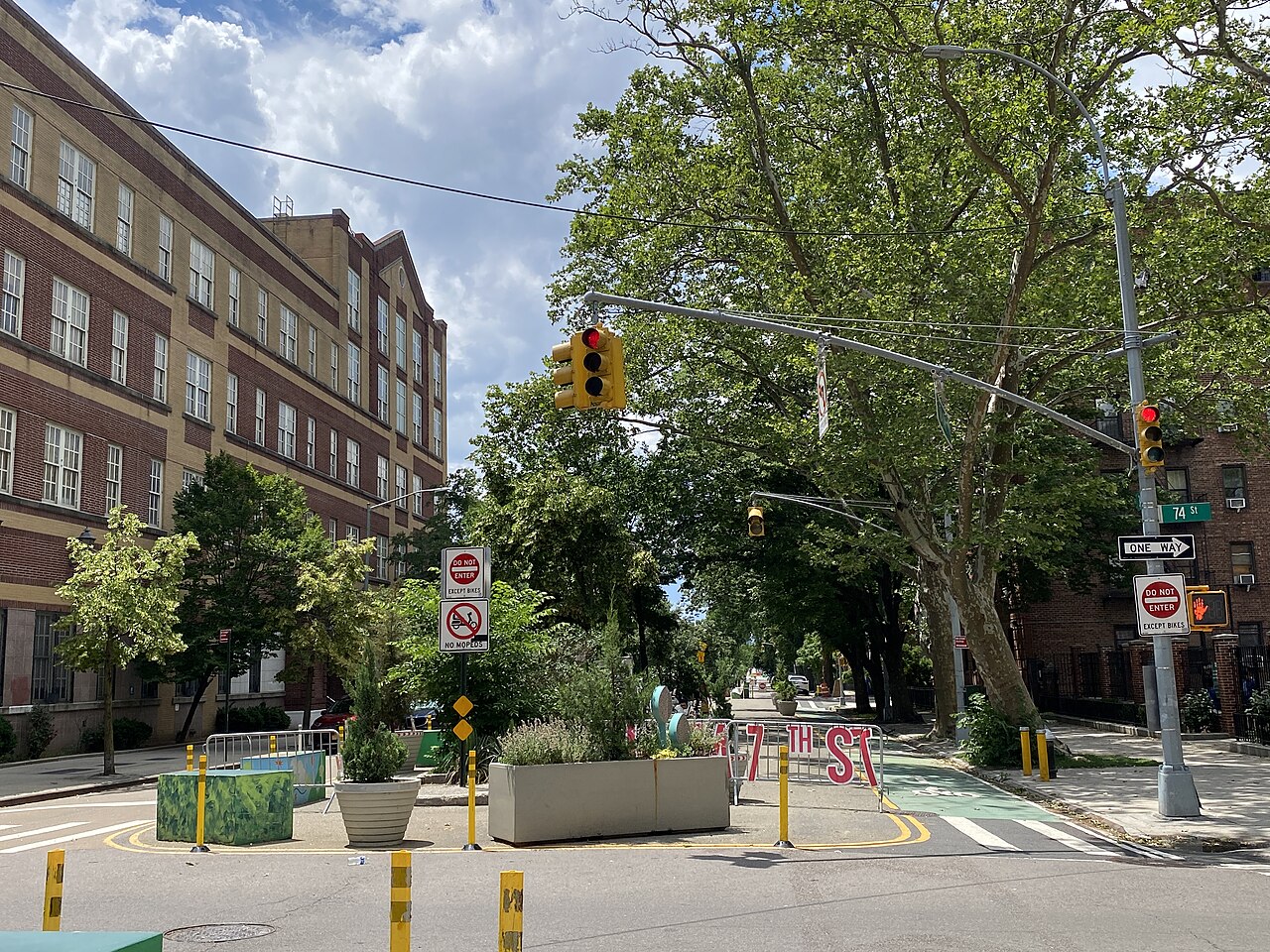 Tree-lined street with a brick school building and a planted open street in Jackson Heights, Queens