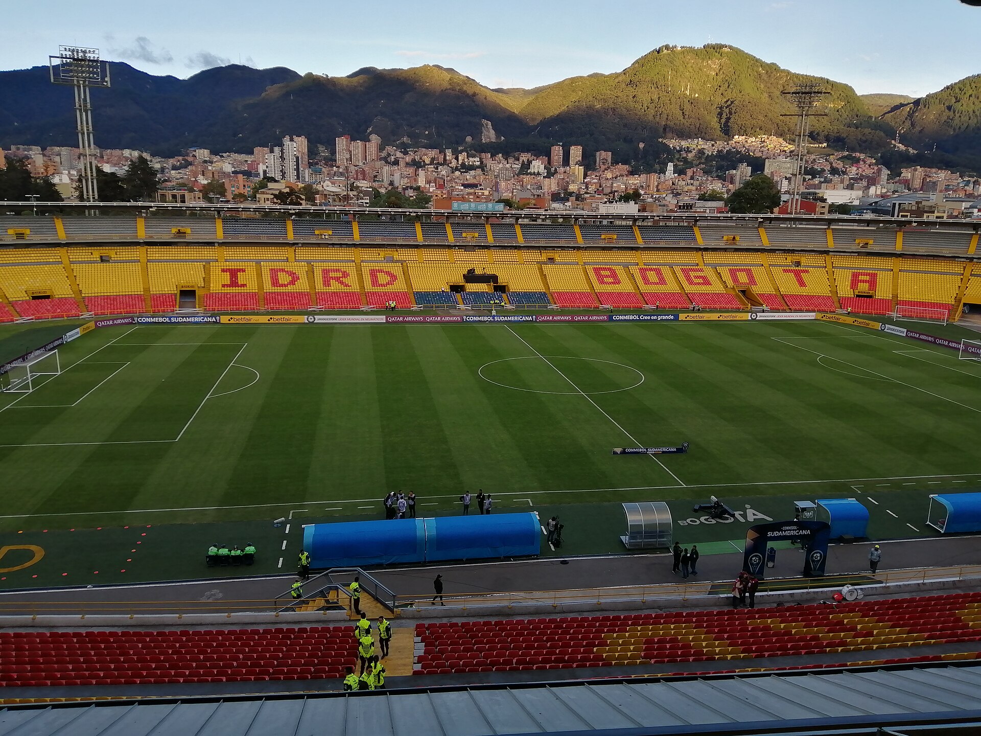The empty pitch at Estadio El Campín in Bogotá, with IDRD lettering in the stands and the eastern hills behind