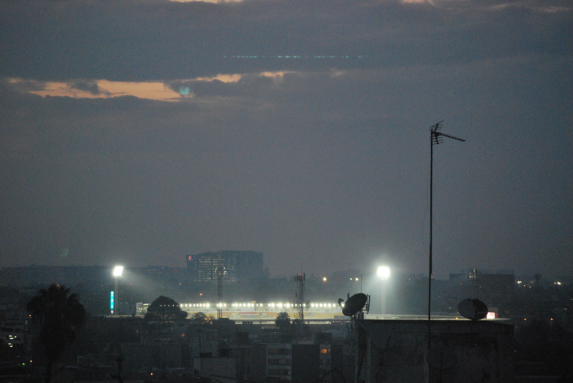 Floodlit Estadio El Campín seen at dusk across the rooftops of Bogotá, Colombia