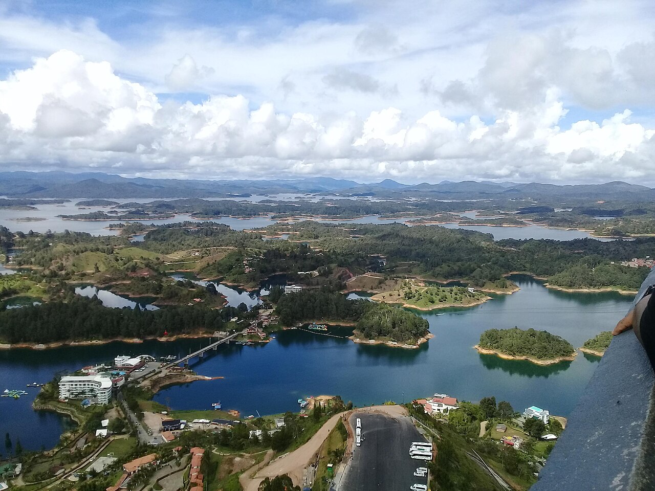 View over the Peñol-Guatapé reservoir in Antioquia, Colombia, with blue water, green islands, a bridge and hills under a cloudy sky