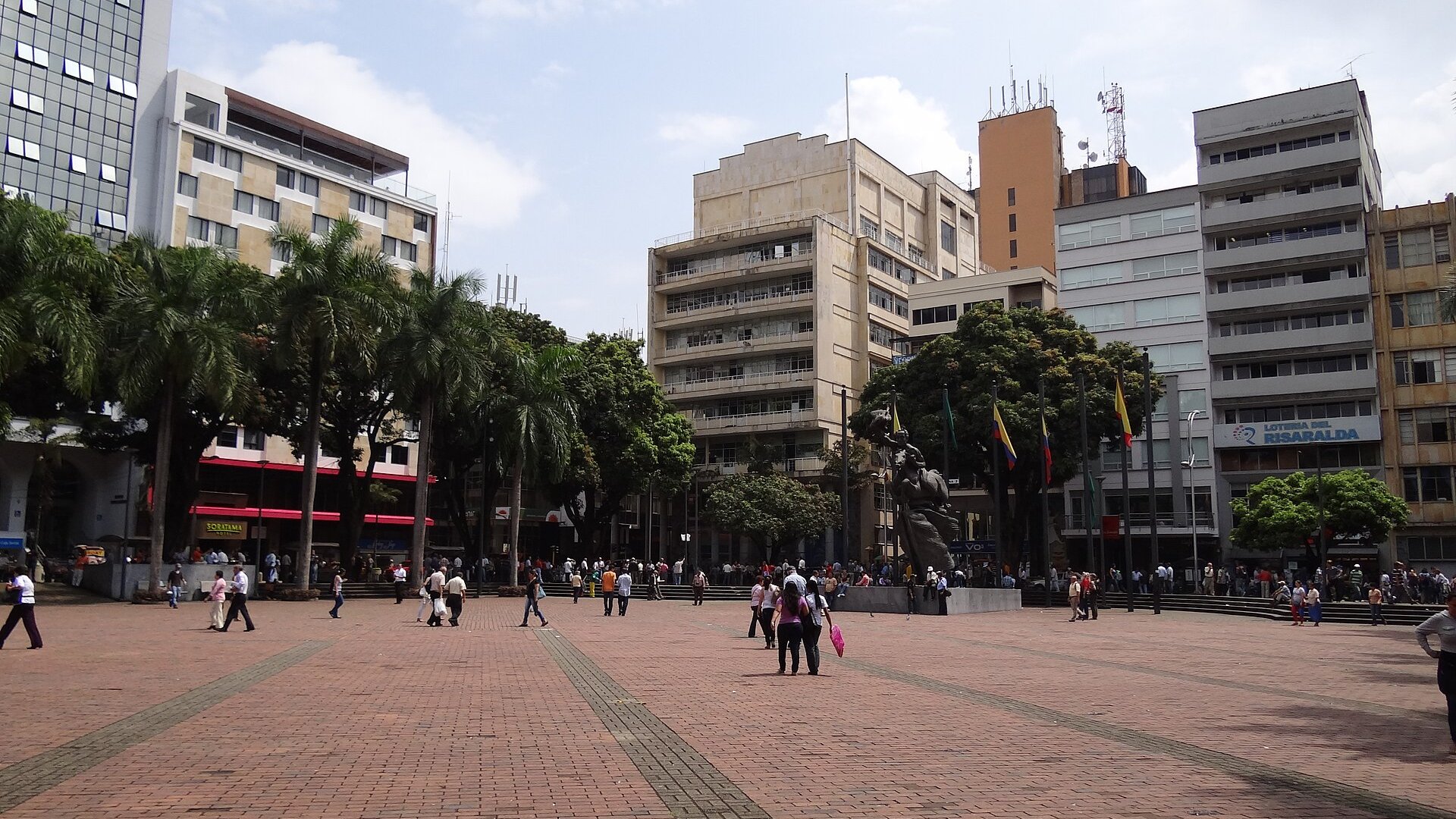 Pedestrians cross the brick Plaza de Bolivar in Pereira, Colombia, with the Bolivar statue and office buildings behind