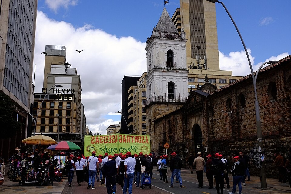 Trade union members in red caps march on May Day along Carrera Séptima in central Bogotá, Colombia