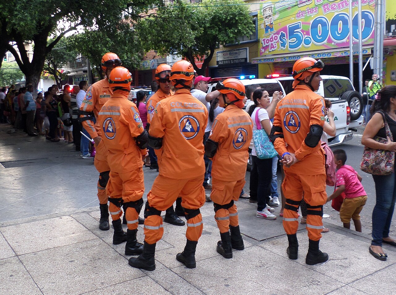 Civil defence volunteers in orange uniforms standing on a busy street in Cúcuta, Colombia