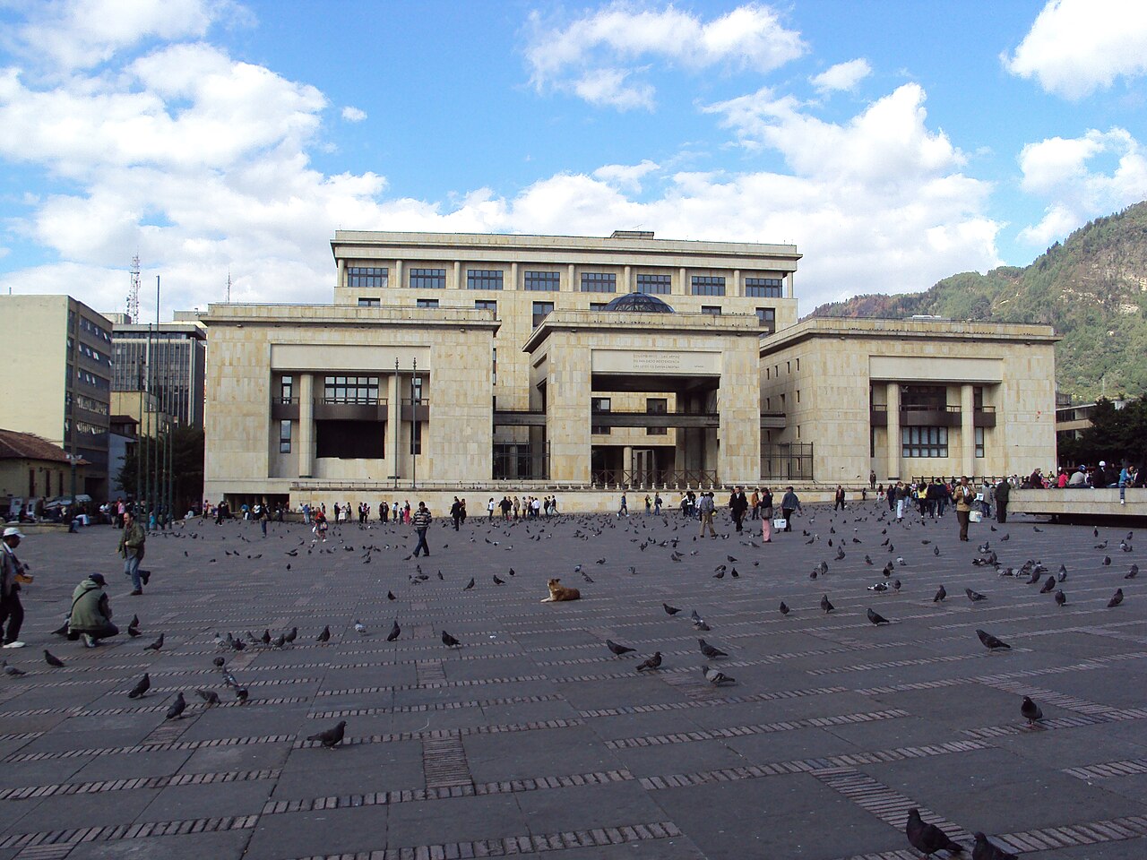 The Palace of Justice seen across Bolívar Square in Bogotá, with pigeons on the paving and a green mountain slope behind