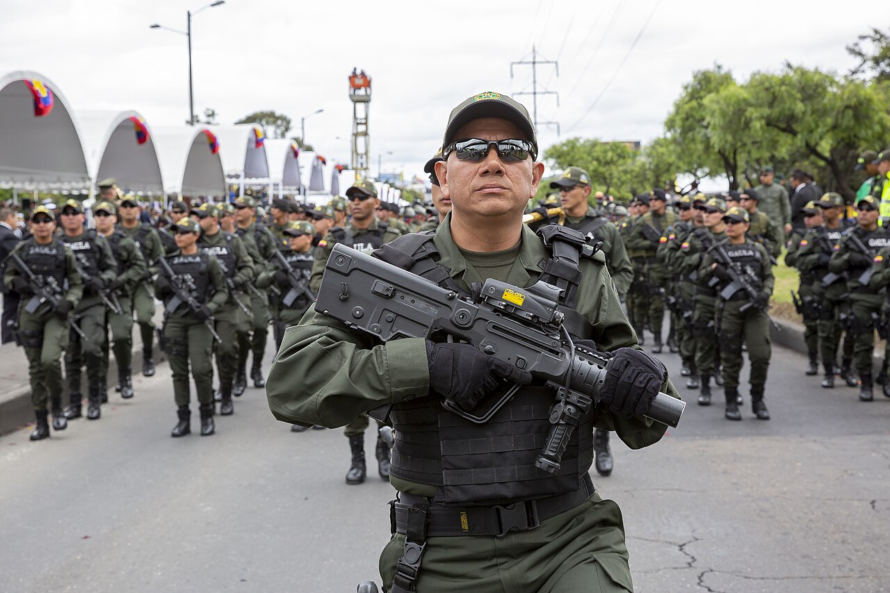 Colombian police officers in green uniforms and body armour march with rifles along a road during a parade
