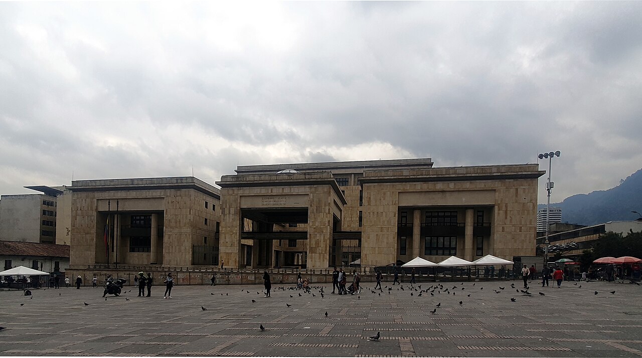 Modern stone Palace of Justice across a wide square with pigeons and pedestrians in Bogotá under grey clouds