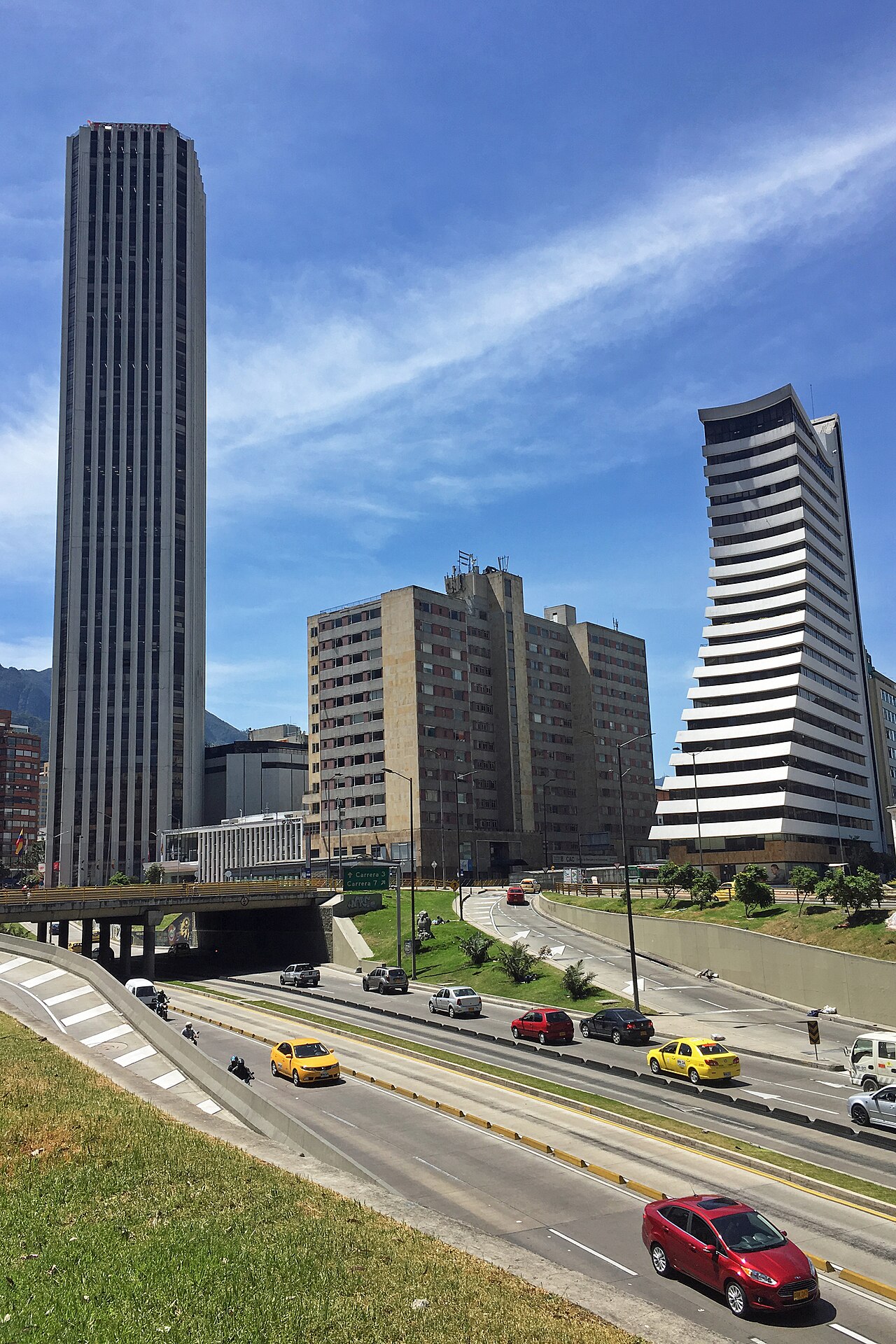 The Torre Colpatria tower beside other office buildings above a busy Bogotá avenue with taxis and cars under a blue sky