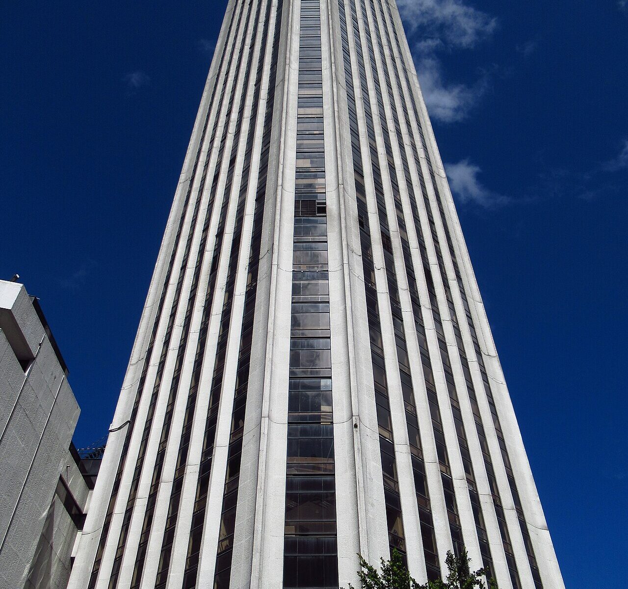 The Torre Colpatria office tower in Bogotá seen from street level, its white vertical ribs rising against a deep blue sky
